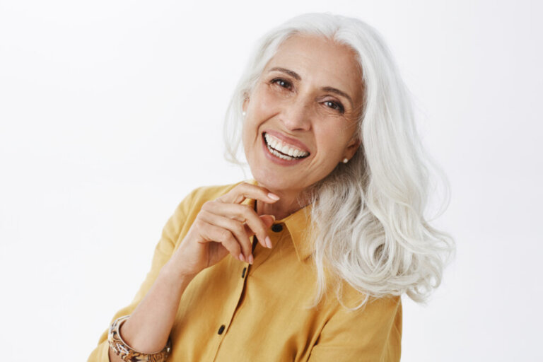 Close-up shot of happy delighted and accomplished charming european elderly female with white hair in yellow trench coat touching face gently laughing from joy feeling pretty and energized