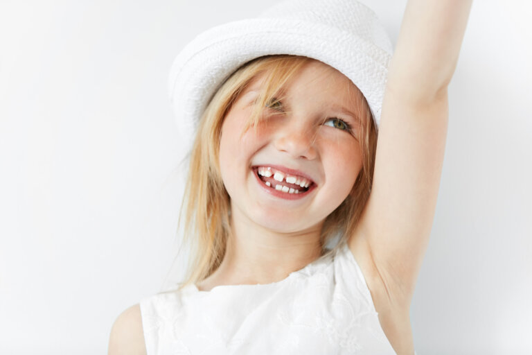 Blond little girl in white morning light stretching her arm up in cheerful mood like celebrating her victory. Smiling child looking up showing her infant teeth and positive emotions